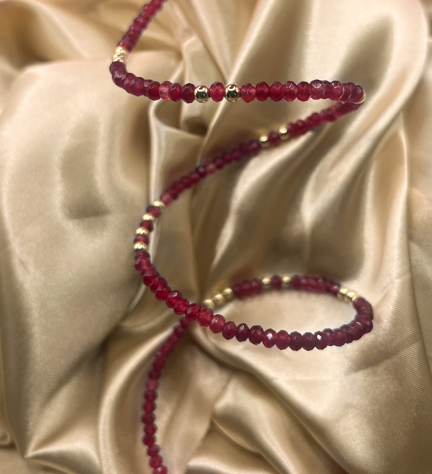 Red beaded bracelet with gold accents on beige fabric. AGATE stone