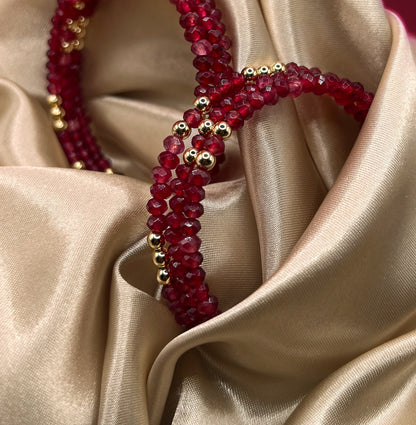 Red beaded bracelet with gold accents on beige fabric. AGATE stone