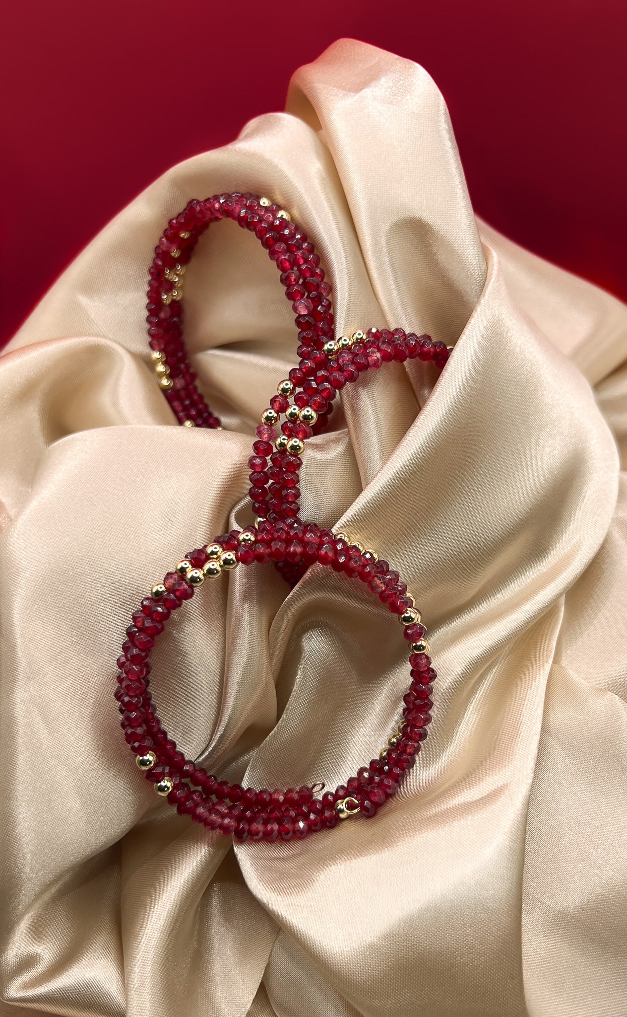 Red beaded bracelet with gold accents on beige fabric. AGATE stone