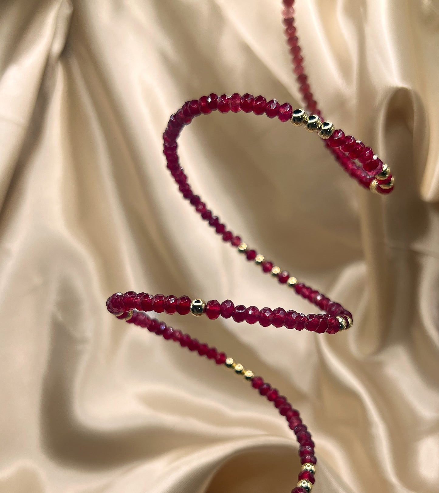 Red beaded bracelet with gold accents on beige fabric. AGATE stone