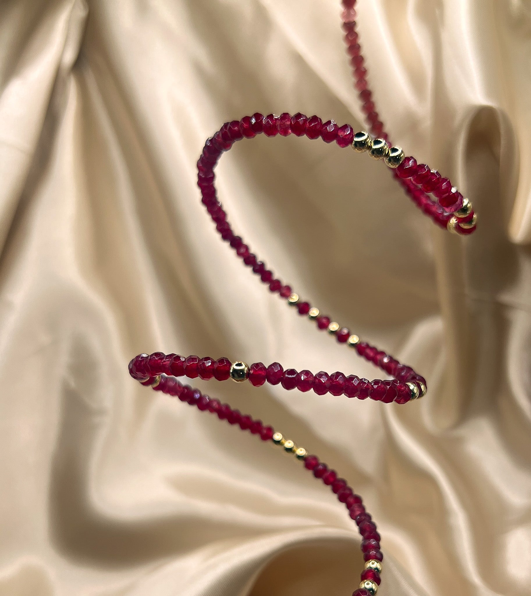 Red beaded bracelet with gold accents on beige fabric. AGATE stone