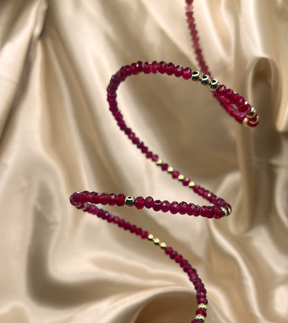 Red beaded bracelet with gold accents on beige fabric. AGATE stone
