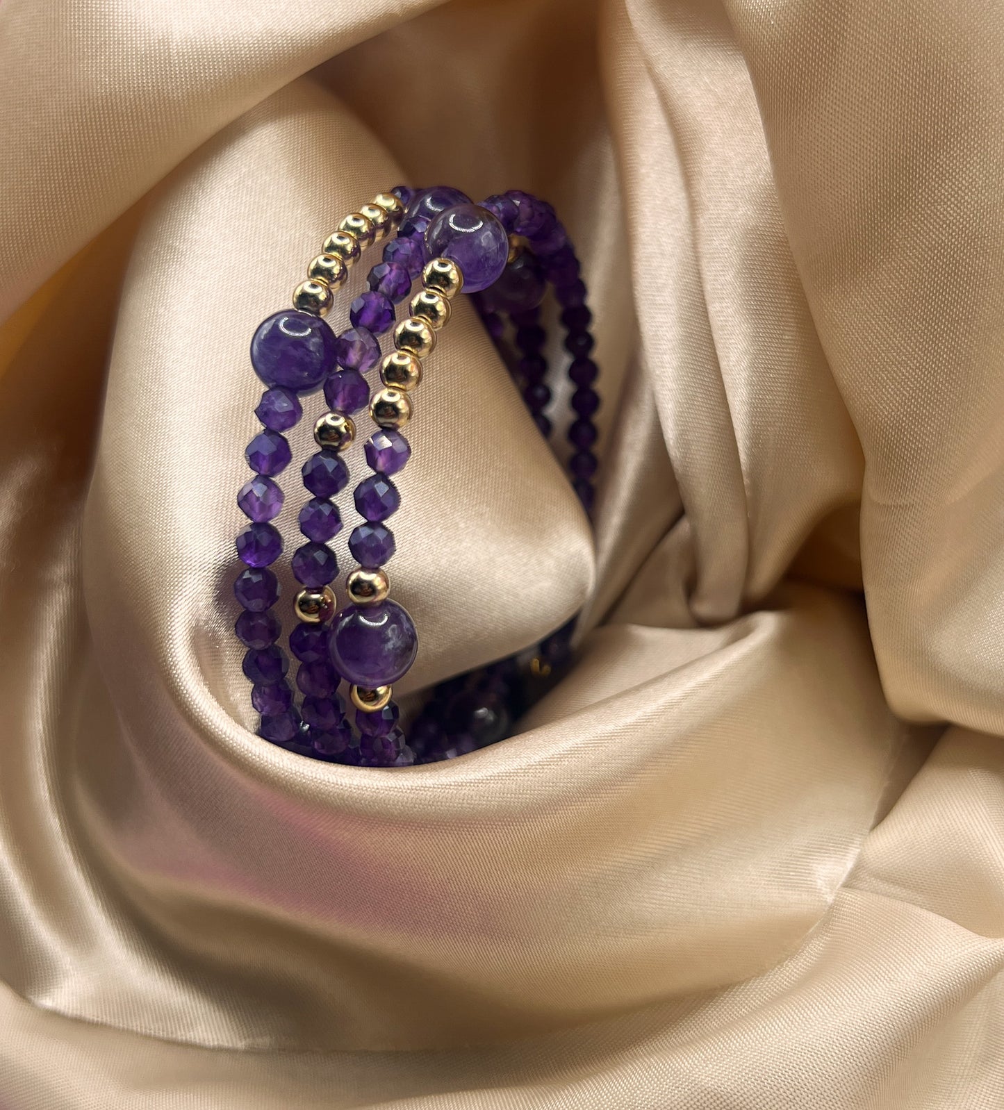 Purple beaded bracelet with gold accents on a beige satin background. Amethyst Stone.