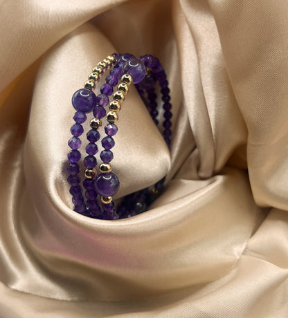 Purple beaded bracelet with gold accents on a beige satin background. Amethyst Stone.