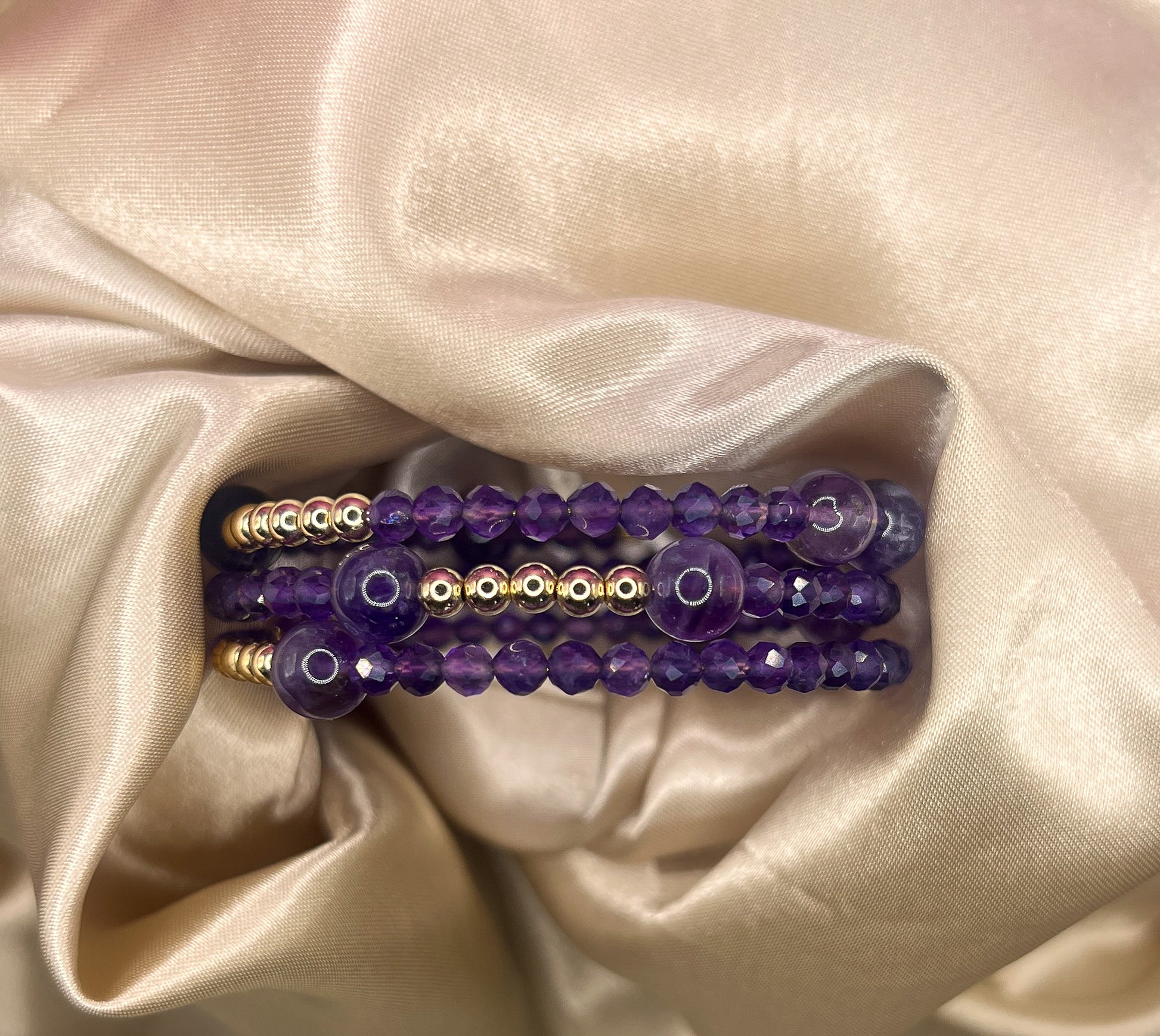 Purple beaded bracelet with gold accents on a beige satin background. Amethyst Stone.