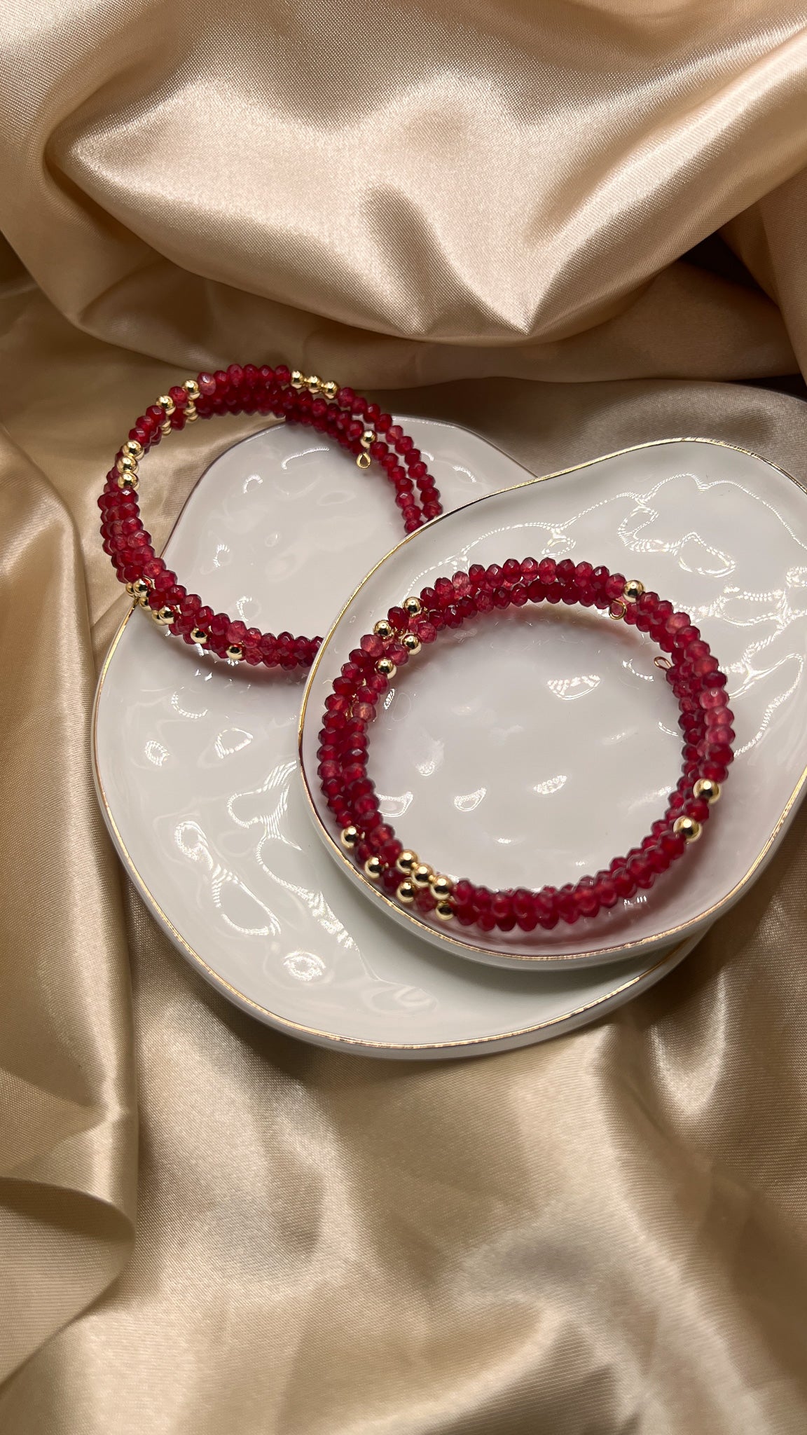 Red beaded bracelet with gold accents on beige fabric. AGATE stone